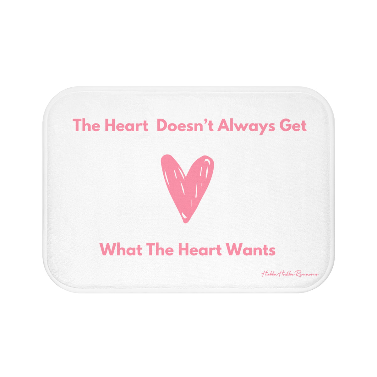 This bath mat features a clean white background with soft pink text and a large pink heart illustration at its center. The top line reads: “The Heart Doesn’t Always Get,” and the bottom line finishes the sentence: “What The Heart Wants.” The heart is hand-drawn in a casual, playful style. The overall design is minimalist and emotionally expressive. The mat features a soft, absorbent surface ideal for bathroom use, especially for romance readers who appreciate a touch of heartbreak with their hygiene.
