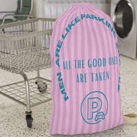 This laundry bag features a pink background with vertical pastel-pink stripes. Centered, bold, teal text reads: "All the good ones are taken." Above the text, in a large curved arc, it says: “Men are like parking spaces!” Below the quote is a parking symbol: a capital letter “P” inside a circle with a car icon in the corner. The bag includes a drawstring closure and a canvas carrying strap. The tone is playful, retro, and full of tongue-in-cheek charm. It is placed in front of a cart for size context
