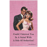 The image features a vintage-style illustration of a sophisticated couple from the 1950s. The woman, styled with glamorous makeup and a bouffant hairstyle, wears a pink dress with floral embroidery, while the man, exuding charm, is dressed in a sleek, dark suit and stands close behind her. Above them, text reads: "Could I Interest You In A Salad With A Side Of Seduction?" This design blends retro fashion with a playful, romantic flair, ideal for adding a touch of nostalgic elegance and wit to any setting. 