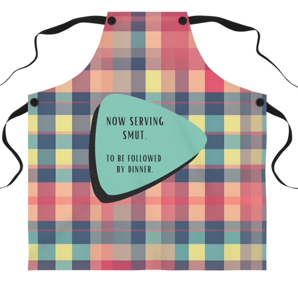 A colorful plaid apron with black straps features a retro-inspired teal and black geometric shape containing the text: "Now serving smut. To be followed by dinner."
