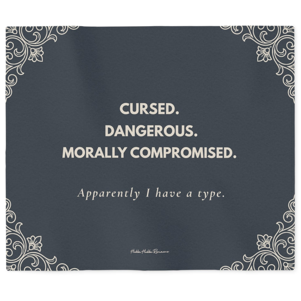 Slate gray sweatshirt blanket featuring the quote "Cursed. Dangerous. Morally Compromised. Apparently I have a type." with elegant gothic corner flourishes. The font and the corner flourishes are in a cream color.