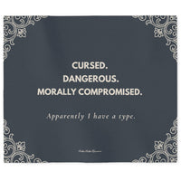 Slate gray sweatshirt blanket featuring the quote "Cursed. Dangerous. Morally Compromised. Apparently I have a type." with elegant gothic corner flourishes. The font and the corner flourishes are in a cream color.