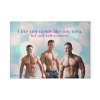 Glass cutting board featuring three shirtless, muscular men smiling confidently against a soft, pastel bokeh background. Above them, the text reads: “i like my meals like my men. hot and well-seasoned.” Made of durable tempered glass with a textured surface and non-slip rubber feet. This is the smaller size. 