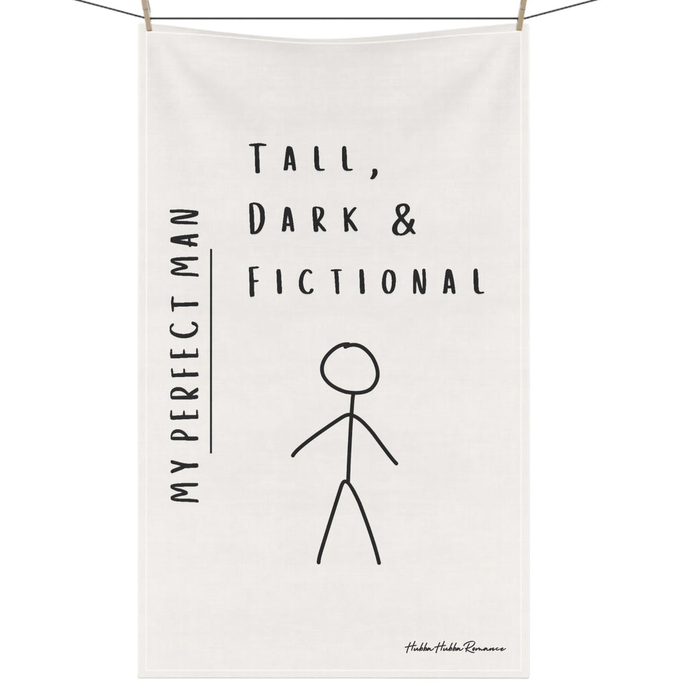 An off-white kitchen towel featuring an image of a male stick figure along with the words: My Perfect Man. Tall, Dark, and Fictional hangs on a clothesline secured by clothespins.
