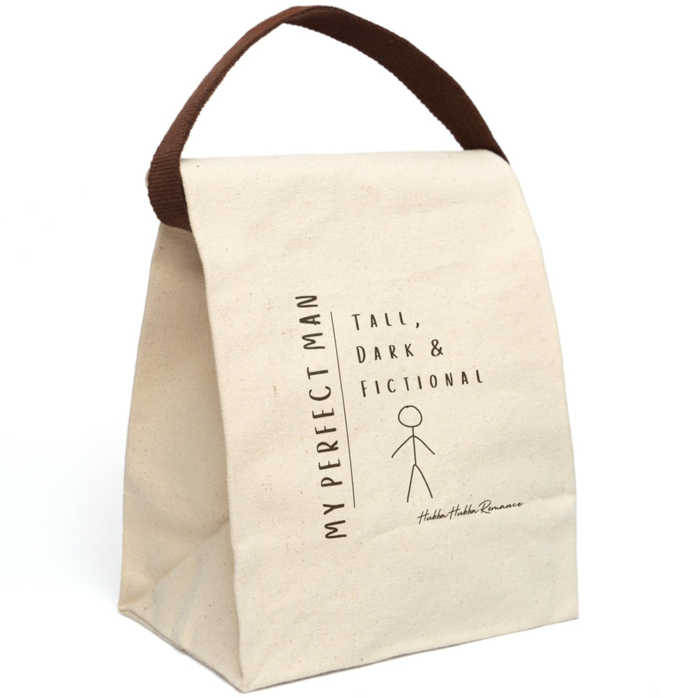 This canvas lunch bag features a minimalist, hand-drawn design on a plain canvas background. On the left, vertical text reads “MY PERFECT MAN.” To the right, in a casual handwritten font, it says: “Tall, Dark & Fictional.” Below the text is a simple brown stick figure drawing of a man. The design is playful and tongue-in-cheek. The bag includes a durable canvas body, roll-top enclosure, and strap—ideal for everyday use by book lovers and romance readers. The strap is displayed upright.