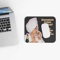 A rectangular mouse pad with rounded corners sits on a white surface next to a cropped silver laptop. The mat has a black background with a printed graphic of a woman wrapped in a white towel and holding a phone, plus the text 'Romance Crisis Line?' and a white computer mouse placed on top.
