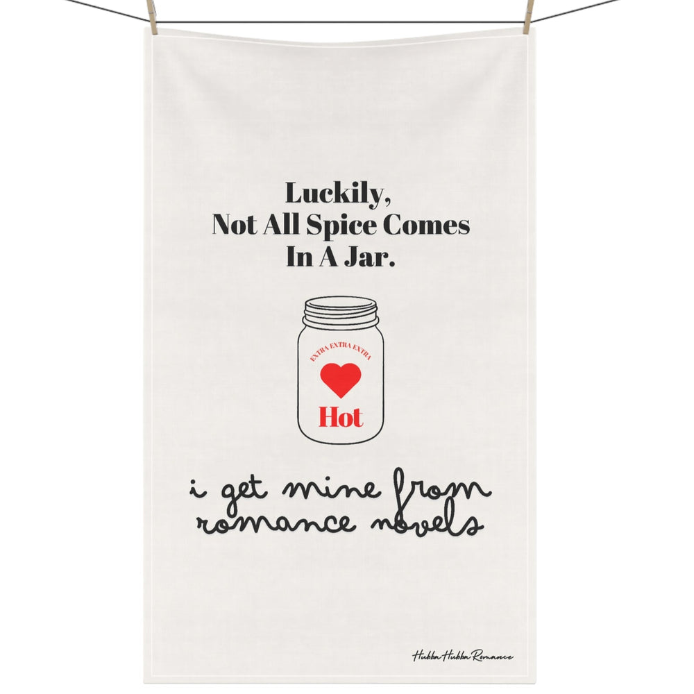 Picture of a kitchen towel hanging on a clothesline with clothespins. The towel features an outline drawing of a mason jar. In the center of the jar are the words “extra, extra, extra” over a red heart with the word “hot” under the heart. The text on the towel says: “Luckily, not all spice comes in a jar. Think Romance Novels.”