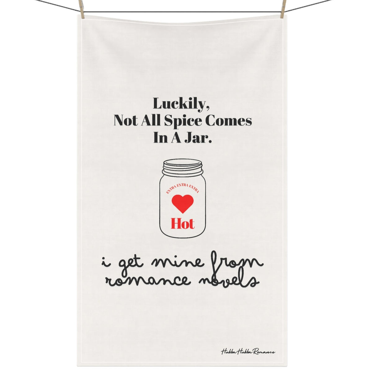 Picture of a kitchen towel hanging on a clothesline with clothespins. The towel features an outline drawing of a mason jar. In the center of the jar are the words “extra, extra, extra” over a red heart with the word “hot” under the heart. The text on the towel says: “Luckily, not all spice comes in a jar. Think Romance Novels.”