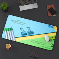 The desk mat is displayed with a laptop nearby and a mouse on it, with assorted office items lying on the desk as well.
