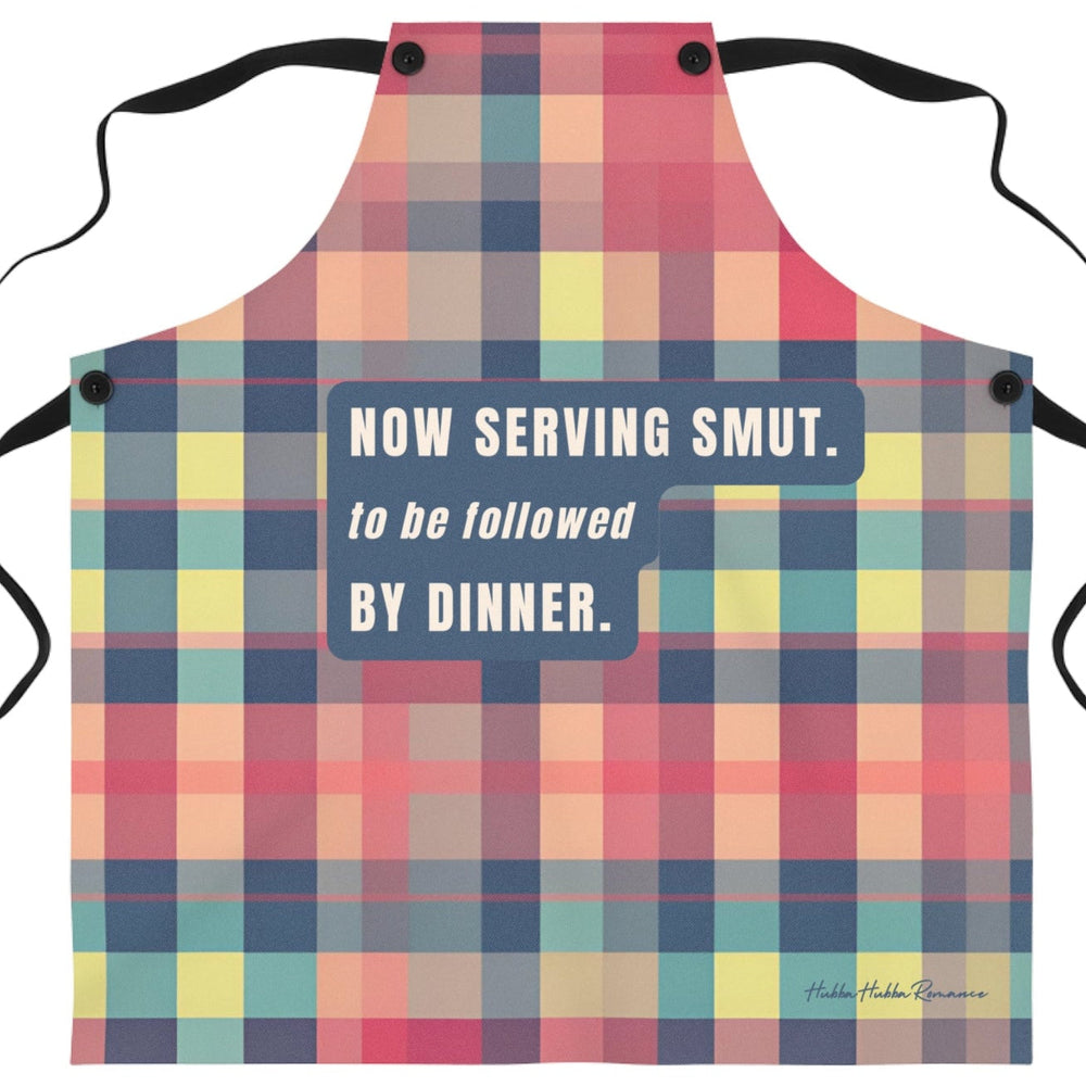 A novelty kitchen apron with a colorful plaid pattern in pink, red, yellow, and blue, featuring the humorous text 'NOW SERVING SMUT. to be followed BY DINNER.