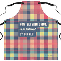 A novelty kitchen apron with a colorful plaid pattern in pink, red, yellow, and blue, featuring the humorous text 'NOW SERVING SMUT. to be followed BY DINNER.
