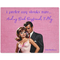 The image depicts a stylized vintage illustration of a glamorous couple. The woman, with voluminous brunette hair and a white evening gown, leans affectionately against a man in a sleek black suit. The background is a textured pink fabric, enhancing the retro aesthetic. Above them, playful text in cursive reads, "i prefer my steaks rare... and my Book Boyfriends Filthy." The design blends romance and humor, appealing to those who enjoy a touch of playful naughtiness in their literary tastes.