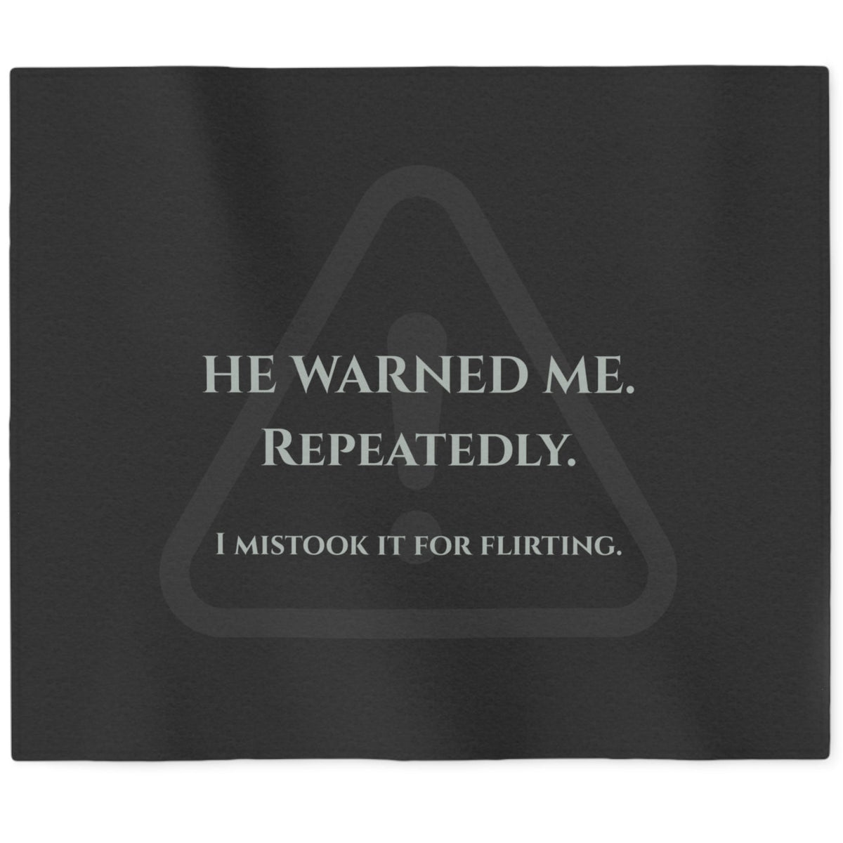 A black rectangular sweatshirt blanket with a gray warning-triangle graphic and the text 'HE WARNED ME. REPEATEDLY. I mistook it for flirting.