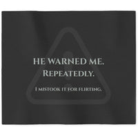 A black rectangular sweatshirt blanket with a gray warning-triangle graphic and the text 'HE WARNED ME. REPEATEDLY. I mistook it for flirting.