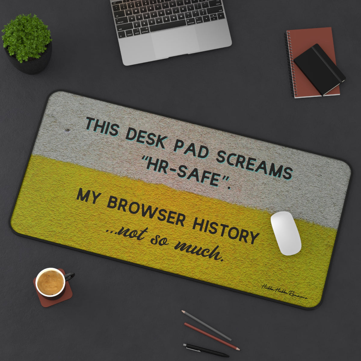 The desk mat is displayed with a laptop nearby and a mouse on it, with assorted office items lying on the desk as well.
