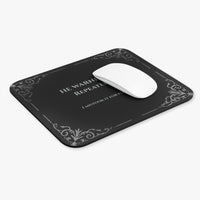 A white computer mouse sits on a rectangular black mouse pad with rounded corners, featuring light grey text and light gray filigree corner accents. The text  reads 'HE WARNED ME. REPEATEDLY. I mistook it for flirting.
