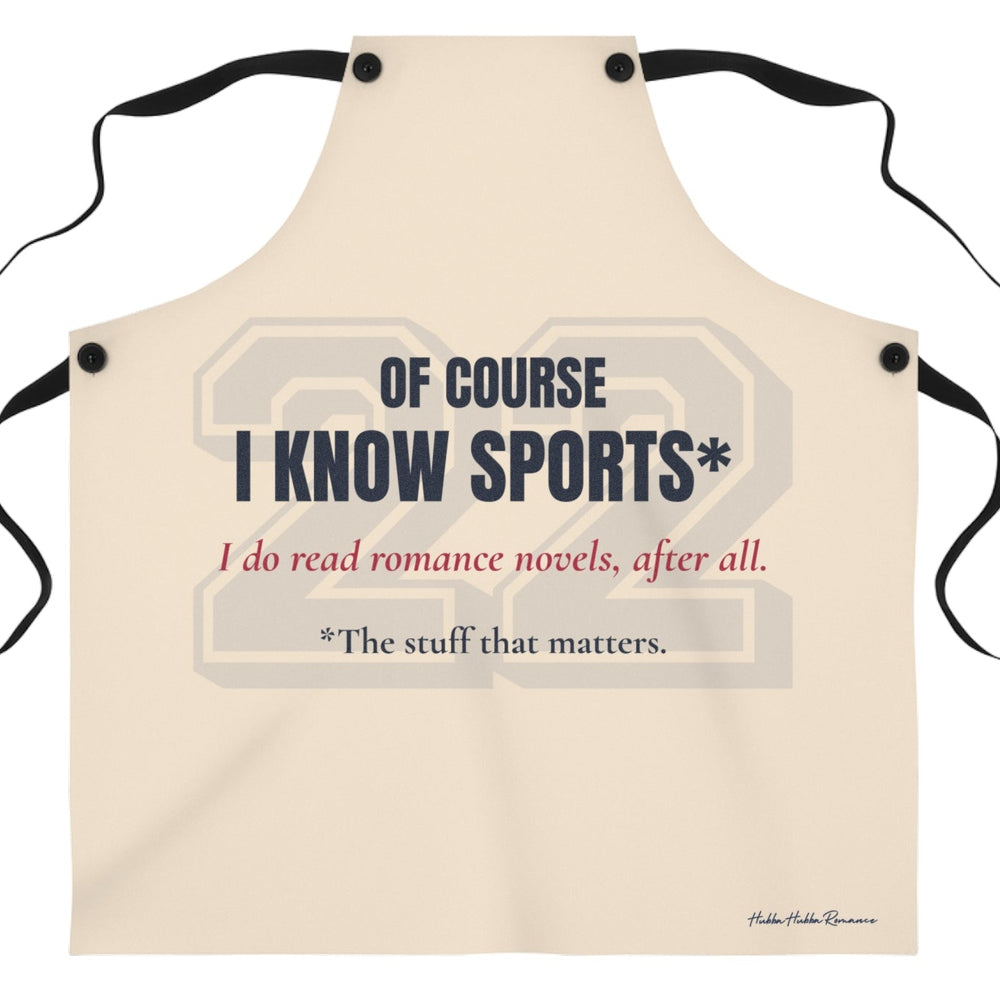  a beige apron that features the text 'OF COURSE I KNOW SPORTS*' in dark blue, with red  text below reading 'I do read romance novels, after all. The last line, in dark blue, reads *the stuff that matters. There is a very faint 22 in a sports font behind the text.