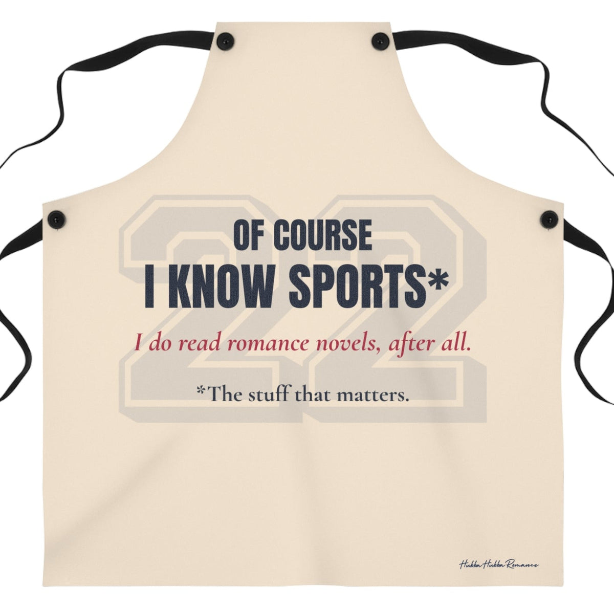  a beige apron that features the text 'OF COURSE I KNOW SPORTS*' in dark blue, with red  text below reading 'I do read romance novels, after all. The last line, in dark blue, reads *the stuff that matters. There is a very faint 22 in a sports font behind the text.