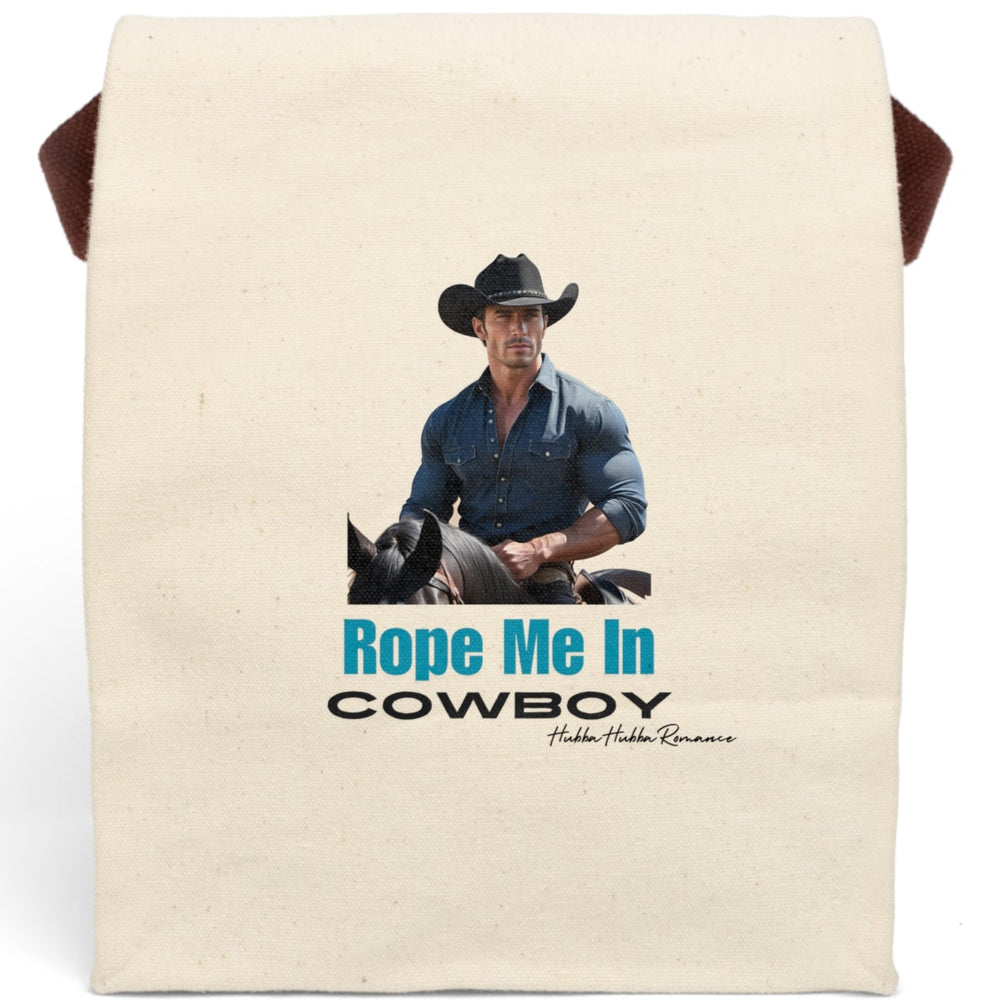 This canvas lunch bag features a full-color image of a muscular, chiseled cowboy riding a black horse. He wears a fitted denim button-down shirt and a black cowboy hat with silver details. His arms are crossed on the saddle, and he gazes ahead with intensity. Below the image, bold turquoise text reads “Rope Me In” followed by black block letters that say “COWBOY.” The bag includes a canvas strap and roll-top closure.