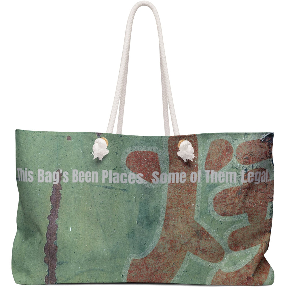 Image features a green and teal distressed background with large, weathered red Asian-style lettering partially visible. Overlaid in bold white type is the phrase “This Bag’s Been Places. Some of Them Legal.” The texture is vintage and gritty, giving the design a mischievous, adventurous vibe. The image is printed on a weekender-style bag, suggesting bold travel, sass, and a hint of trouble. The design is aimed at bold, cheeky romance readers and stylish rule-breakers alike.
