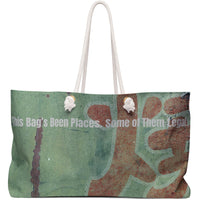 Image features a green and teal distressed background with large, weathered red Asian-style lettering partially visible. Overlaid in bold white type is the phrase “This Bag’s Been Places. Some of Them Legal.” The texture is vintage and gritty, giving the design a mischievous, adventurous vibe. The image is printed on a weekender-style bag, suggesting bold travel, sass, and a hint of trouble. The design is aimed at bold, cheeky romance readers and stylish rule-breakers alike.