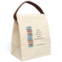 This canvas lunch bag features a playful stack of illustrated romance novels on the left side. Each book spine is brightly colored  with romance tropes as titles like “My Fake Fiancé,” “Secret Baby Daddy,” “Mafia Princess,” “Sexy Silver Fox,” and more. To the right of the stack, bold black typewriter-style text reads: “EAT LUNCH WITH A BOOK BOYFRIEND.” The background is a natural canvas. There is a brown canvas strap for carrying, which is displayed upright.