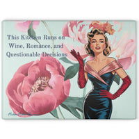 Glass cutting board with a watercolor floral background featuring pink peonies. A retro glamour woman in a strapless black and pink dress with long red gloves stands at the side. The text reads: “This kitchen runs on wine, romance, and questionable decisions.” Made of tempered glass with non-slip rubber feet for countertop use. This is the larger size.