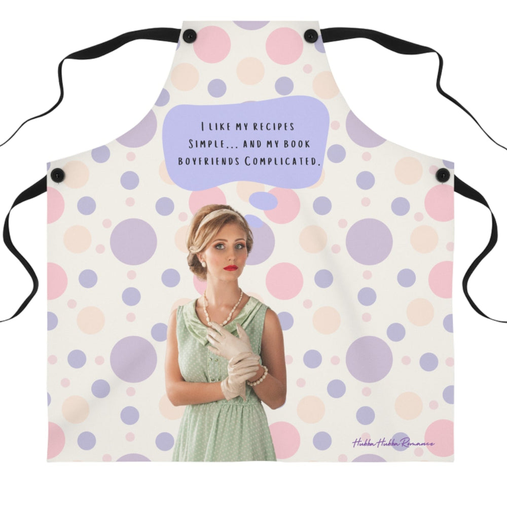 A beige apron with pastel pink and purple polka dots and black straps stands in a modern kitchen. The apron features a vintage-style illustration of a glamorous woman in a mint green dress, pearl necklace, and gloves. Above her, a purple speech bubble contains the text: "I like my recipes simple… and my book boyfriends complicated."
