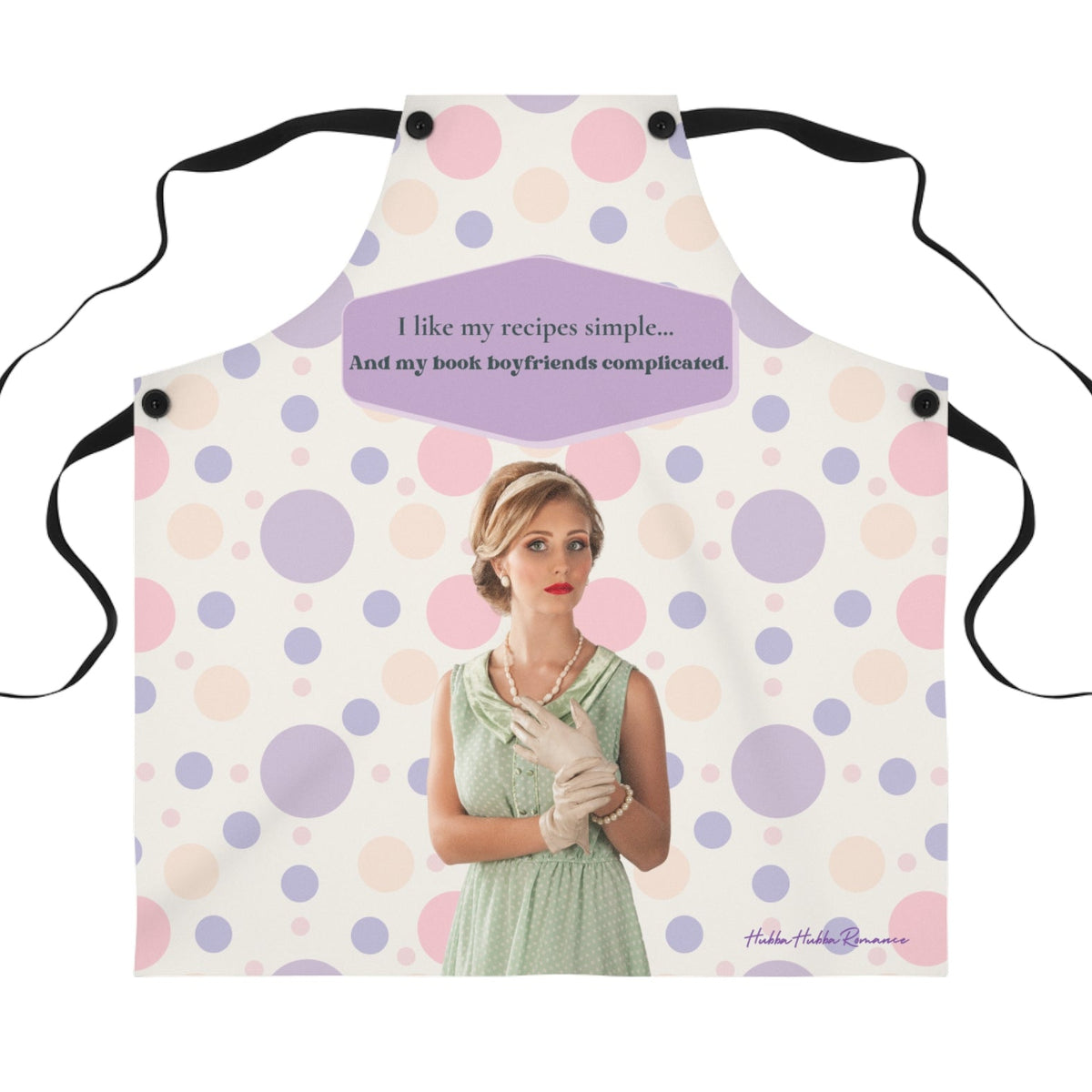White apron with pink and purple polka dots and black straps, vintage-style illustration of woman in mint green dress with pearls and gloves, text reads “I like my recipes simple and my book boyfriends complicated” inside purple speech bubble.