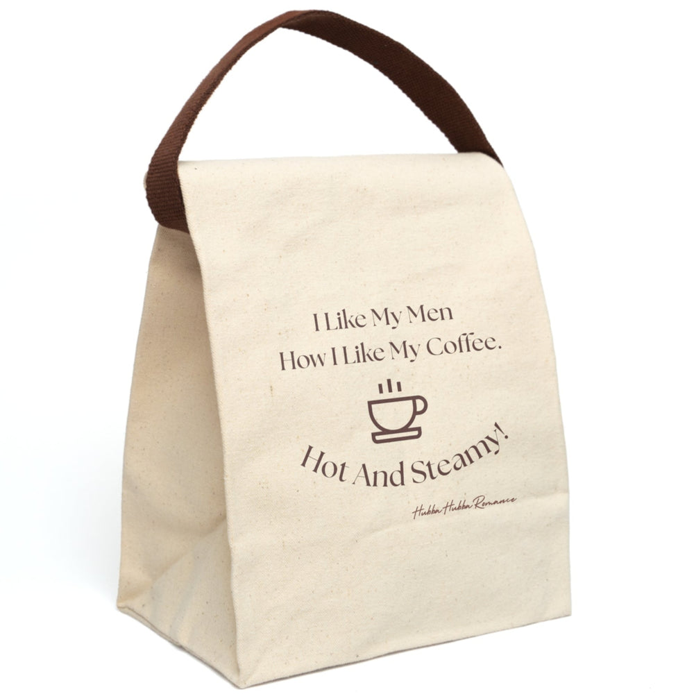 This canvas lunch bag features a white background with brown typography and a simple brown coffee cup icon. The top reads, “I Like My Men How I Like My Coffee.” Below the coffee cup, curved text finishes the joke: “Hot And Steamy!” The design is clean, cheeky, and perfect for coffee lovers and romance readers alike. The bag includes a durable canvas body, roll-top closure, and a carrying strap,which is displayed upright, for easy transport .