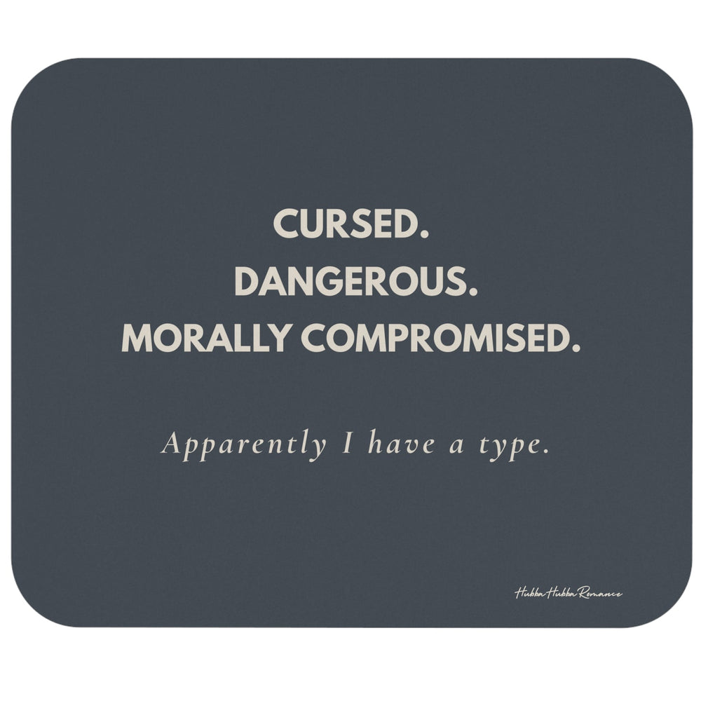 A rectangular dark slate-gray mouse pad with rounded corners, featuring the text 'CURSED. DANGEROUS. Morally Compromised. Apparently I have a type in cream letters.