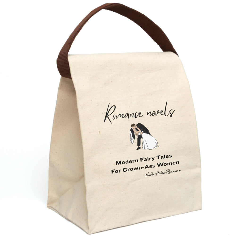 This canvas lunch bag features a plain canvas background with black text. At the top, the words “Romance novels” are written in an elegant script font. Below is an illustration of a bride and groom in a classic dip-kiss pose—the groom in a black suit, the bride in a flowing white gown and veil. Under the image, large bold text reads: “Modern Fairy Tales For Grown-Ass Women.” The design is romantic with a cheeky edge. The bag's canvas strap is displayed upright.