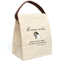 This canvas lunch bag features a plain canvas background with black text. At the top, the words “Romance novels” are written in an elegant script font. Below is an illustration of a bride and groom in a classic dip-kiss pose—the groom in a black suit, the bride in a flowing white gown and veil. Under the image, large bold text reads: “Modern Fairy Tales For Grown-Ass Women.” The design is romantic with a cheeky edge. The bag's canvas strap is displayed upright.