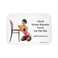 This bath mat showcases a vintage pin-up style image of a woman kneeling beside a wooden chair, engrossed in a book. She is dressed in a pink corset, black lingerie, stockings, and glasses, styled with retro hair and makeup. To the right, bold black text reads: “I Read Steamy Romance Novels For The Plot. Said No One Ever.” The background is solid white, featuring striking text and playful imagery. The mat is soft and absorbent. This is the smallerr size.