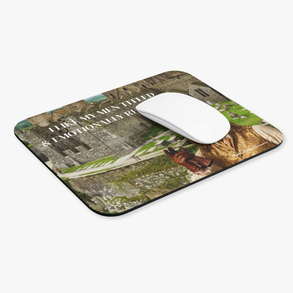 Regency romance mouse pad featuring a handsome aristocratic man in period clothing before a castle with the text “I Like My Men Titled & Emotionally Repressed.” There is a white computer mouse on it.