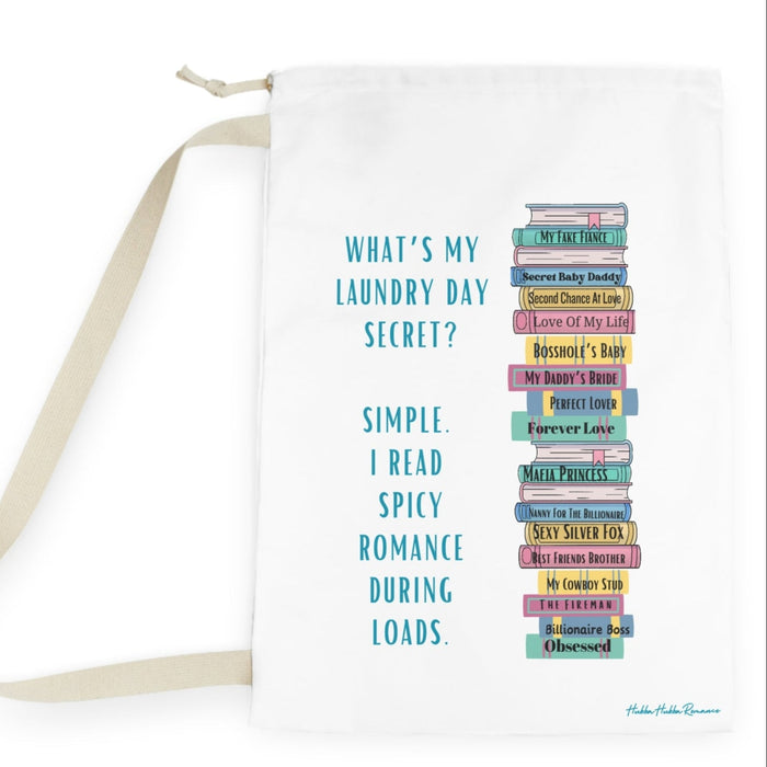 Off-white laundry bag with stack of romance novels graphic and text: “What’s my laundry secret? I read spicy romance during loads.” Drawstring and canvas strap, lying flat.