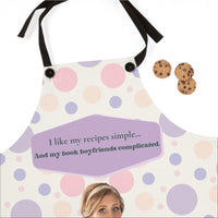Close-up of beige apron with pink and purple polka dots and black straps showing upper portion of design and text.