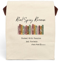 This canvas lunch bag features an illustrated row of romance book spines in muted earth tones, each labeled with tropes or titles like “Surprise Baby,” “Obsession,” “His Secret Fiancé,” “Twin Love,” and “Next Door Love.” Above the books, flowing script reads “Read Spicy Romance.” Below, in bold typewriter-style font, it says: “Packed With Passion And Protein.” The design blends a cheeky tone with a love for books. Bag includes canvas carrying strap and roll-top closure.