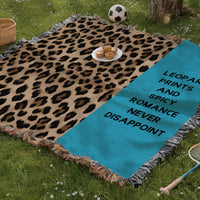 The blanket is being displayed as a picnic blanket in a park setting with a tree stump, picnic basket, plate of muffins, and a tennis racquet and a soccer ball lying around.
