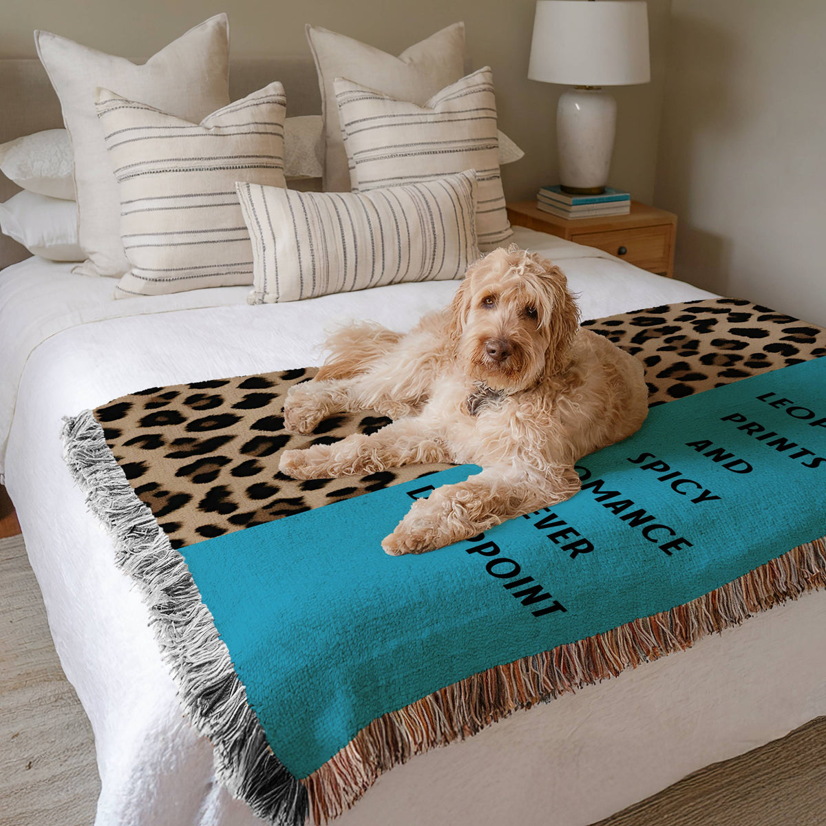 The blanket is displayed neatly folded on a bed with a white bedspread and striped pillows and a large white dog laying on it.
