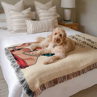 The blanket is displayed neatly folded on a bed with a white bedspread and striped pillows and a large white dog laying on it.

