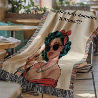 The blanket is displayed lying on a chair in a coffee shop setting with an open book and a cup of coffee on a small round table.

