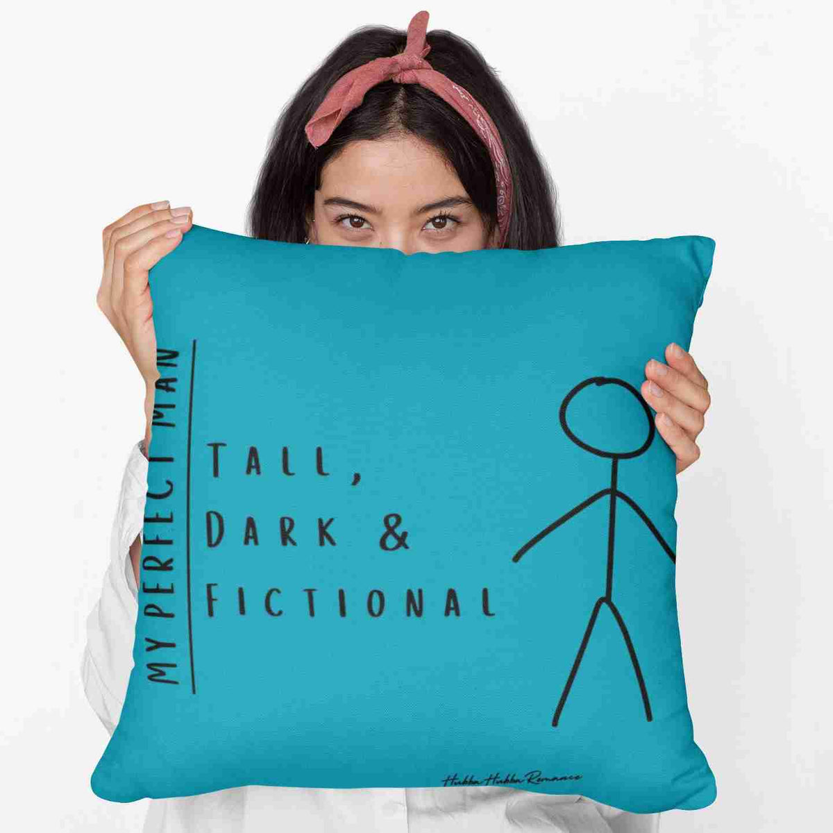 A woman holding a 20-inch turquoise square pillow featuring a stick-figure image of a man and the text, "My Perfect Man. Tall, Dark & Fictional." 

