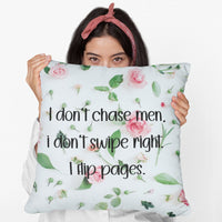 A woman holding a 20 inch pillow featuring an all-over image featuring a small print composition of pink roses, green leaves, and small green buds scattered on a white background. Overlaid in bold, black handwritten-style text is the phrase: "I don’t chase men. I don’t swipe right. I flip pages." The small print floral background gives the image a soft, romantic feel, while the text adds a sassy and book-lover-friendly attitude.