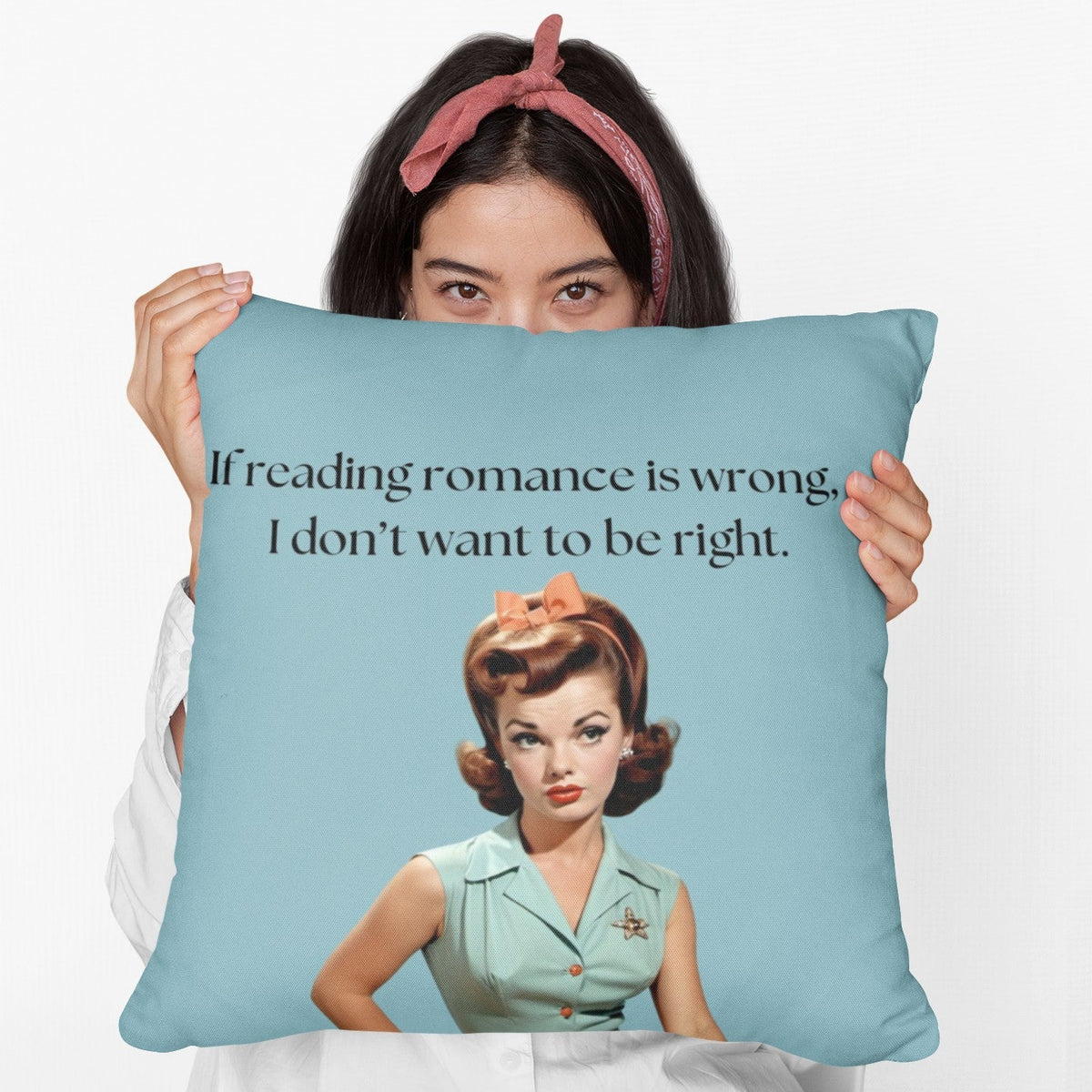 A woman holding a 20-inch pillow featuring a vintage-inspired illustration of a glamorous 1950s woman with red hair styled in curls, wearing a mint green blouse with orange buttons, an orange skirt, a black belt, and a matching orange bow in her hair. She has bold red lipstick and a skeptical expression. The background is a solid teal color. Above her, black text reads: "If reading romance is wrong, I don’t want to be right."
