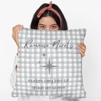 A woman holds a 20-inch pillow featuring a gray and white gingham background with elegant script text that reads: "Romance Novels." Below, in a playful handwritten-style font, the phrase "modern fairy tales for grown ass women" is written. To the left of the text, there are three gray starbursts, adding a touch of vintage charm. The overall design is minimalist yet bold, appealing to romance readers who embrace their love for modern-day fairy tales.