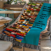 The blanket is displayed lying on a chair in a coffee shop setting with an open book and a cup of coffee on a small round table.
