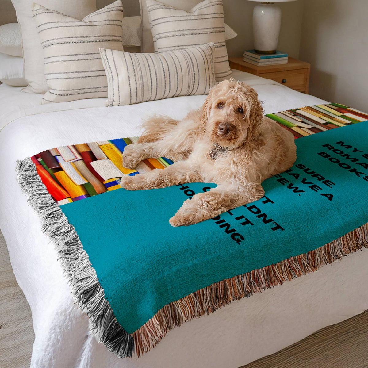 The blanket is displayed neatly folded on a bed with a white bedspread and striped pillows and a large white dog laying on it.

