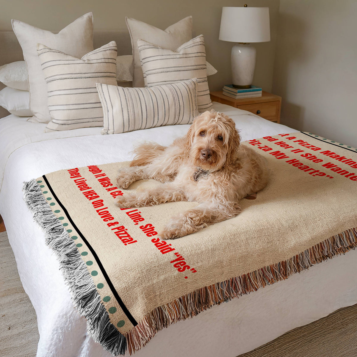 The blanket is displayed neatly folded on a bed with a white bedspread and striped pillows and a large white dog laying on it.
