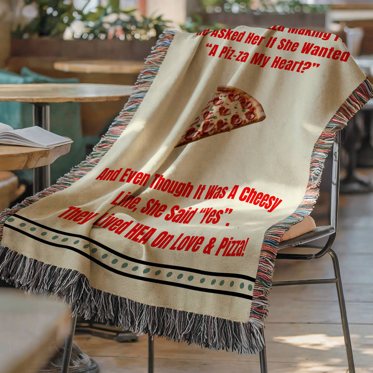 The blanket is displayed lying on a chair in a coffee shop setting with an open book and a cup of coffee on a small round table.
